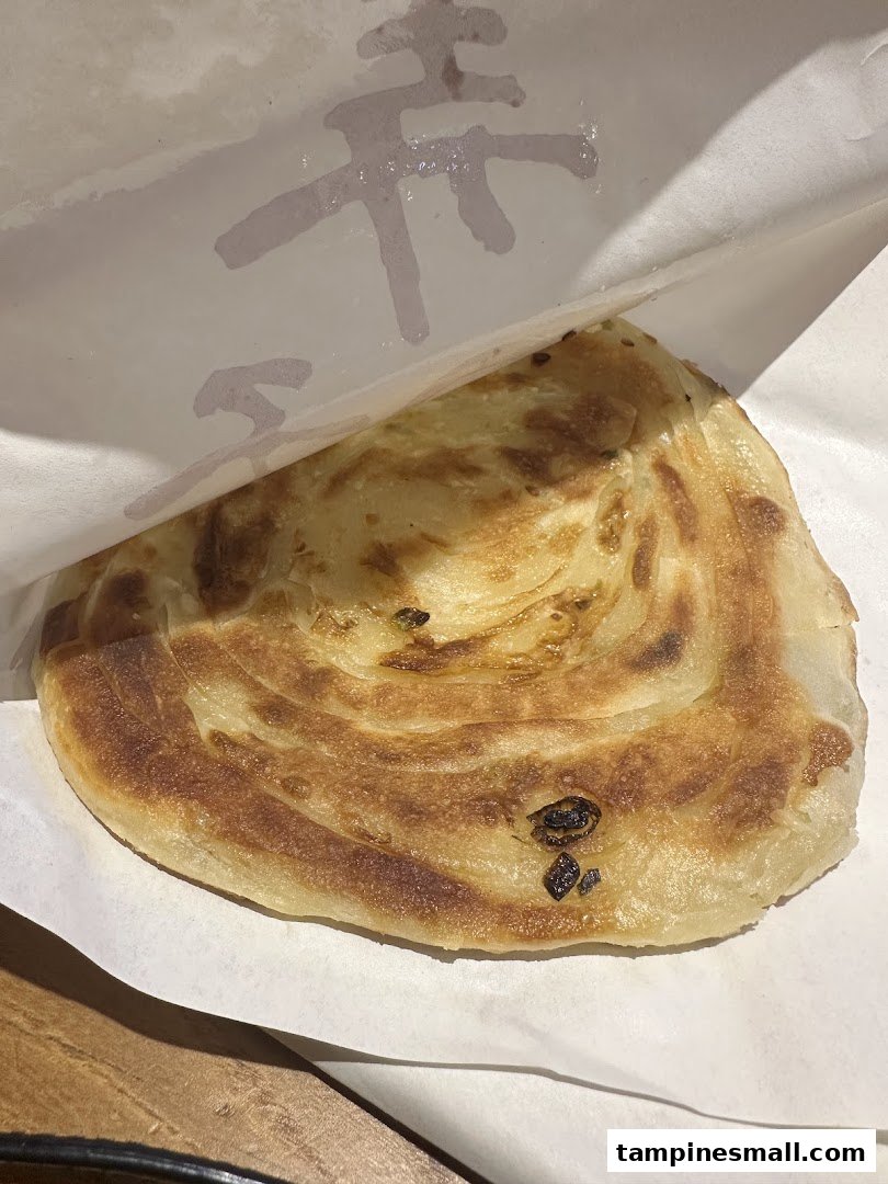 A golden-brown, flaky scallion pancake served in a paper wrapper from Alley Wei.
