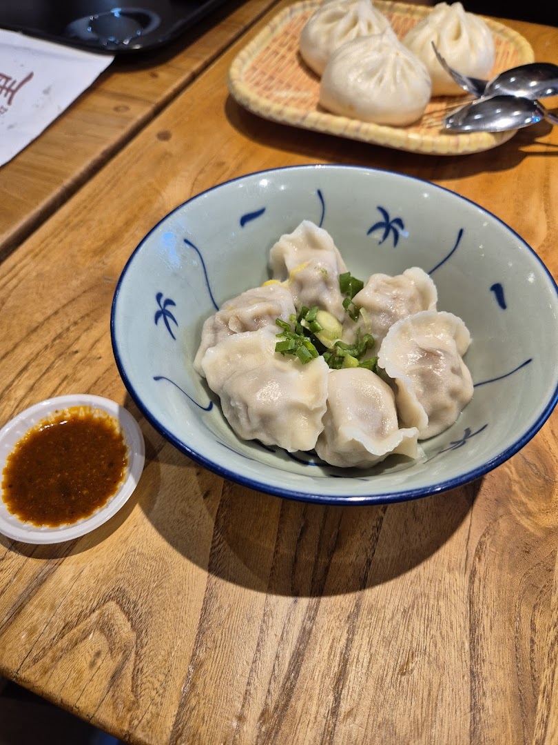 A bowl of freshly prepared dumplings and a plate of steamed buns on a wooden table.