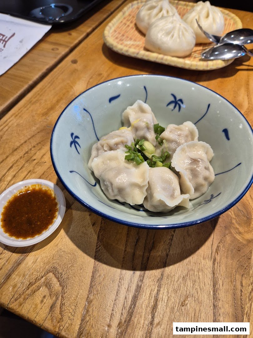 A bowl of freshly prepared dumplings and a plate of steamed buns on a wooden table.