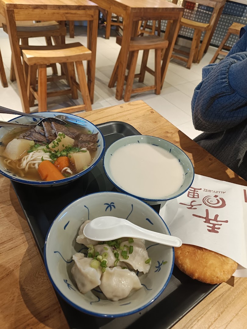 A tray with beef noodle soup, dumplings, a drink, and a fried pastry on a wooden table at Alley Wei.