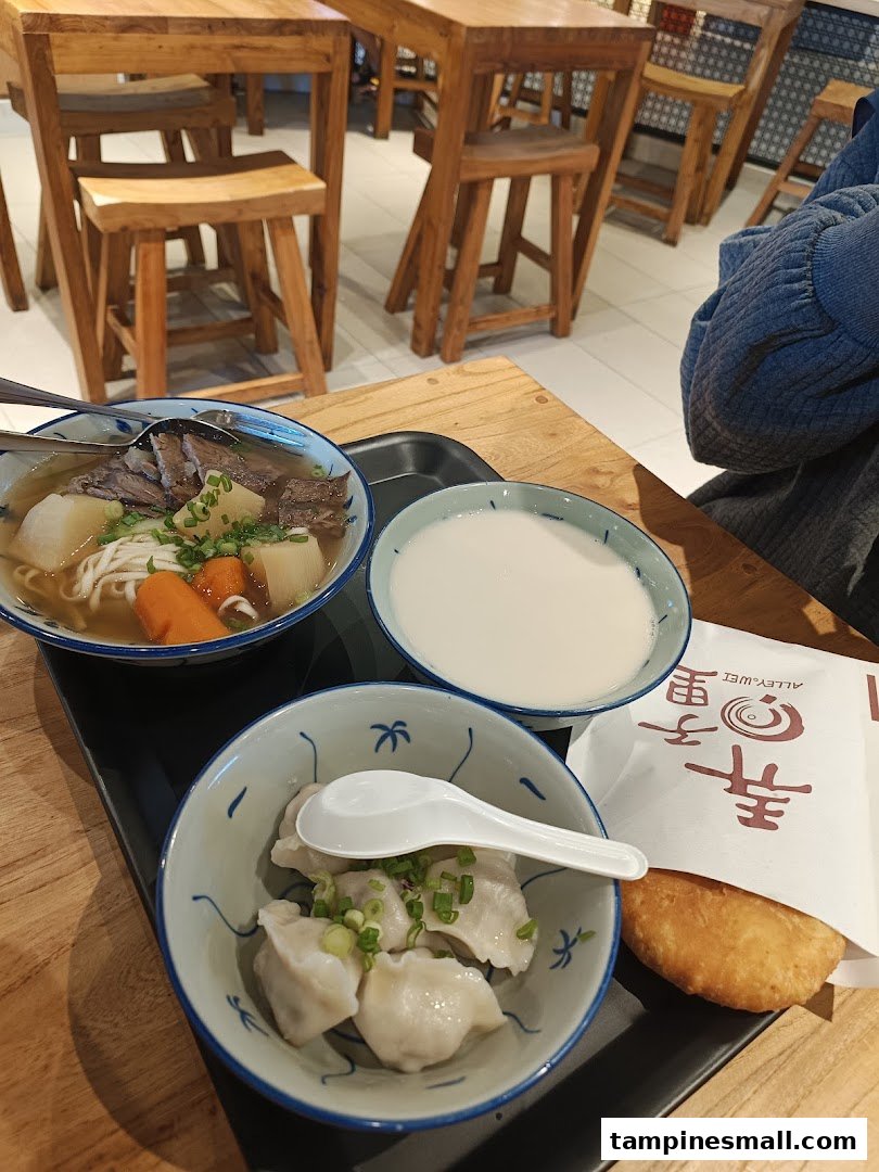 A tray with beef noodle soup, dumplings, a drink, and a fried pastry on a wooden table at Alley Wei.