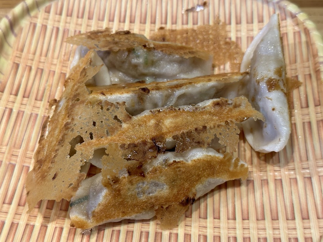 Close-up of pan-fried dumplings with crispy edges, served on a woven bamboo-style mat.