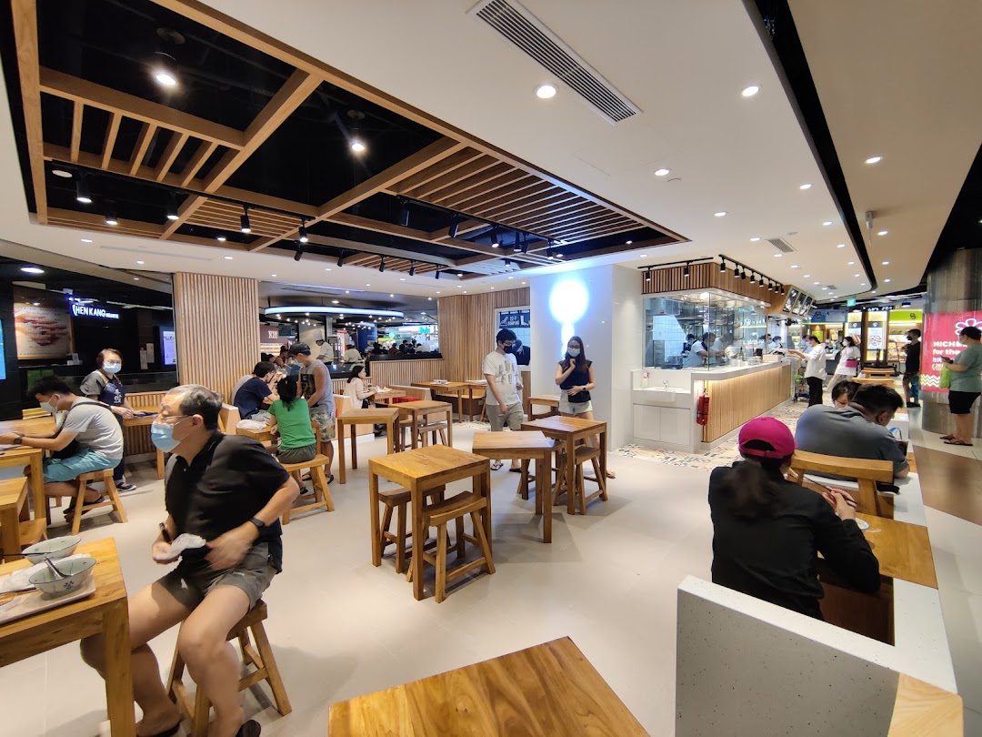 Diners enjoy a bright, modern food court setting with wooden tables and an open kitchen concept.