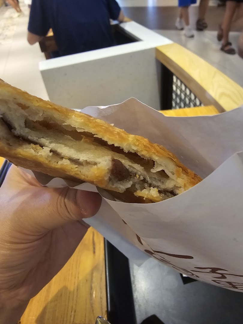 A hand holds a flaky, golden-brown pastry with a savory filling from Alley Wei.