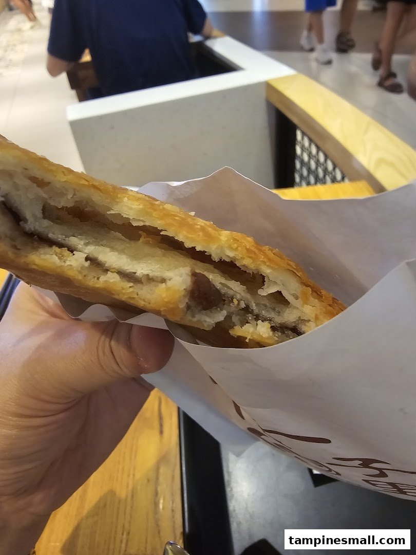 A hand holds a flaky, golden-brown pastry with a savory filling from Alley Wei.