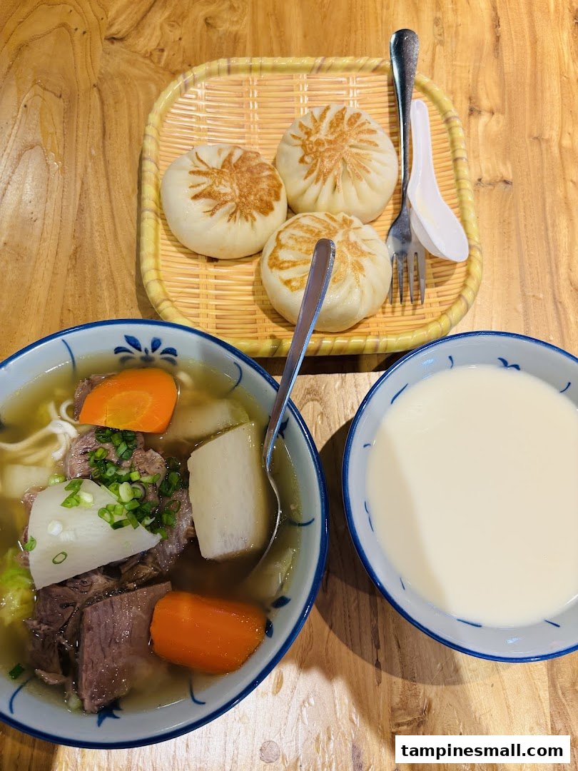 A delicious meal featuring beef noodle soup, pan-fried buns, and a bowl of soy milk on a wooden table.