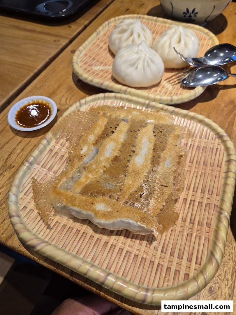 A close-up of crispy pan-fried dumplings and fluffy steamed buns served on bamboo trays.