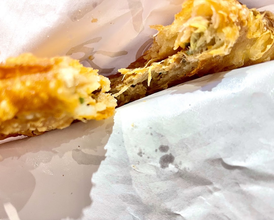 Close-up of a golden-brown, crispy pastry or fried snack, broken open to reveal its savory filling.