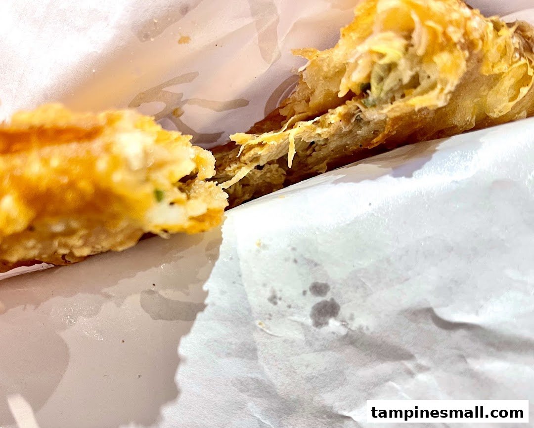 Close-up of a golden-brown, crispy pastry or fried snack, broken open to reveal its savory filling.