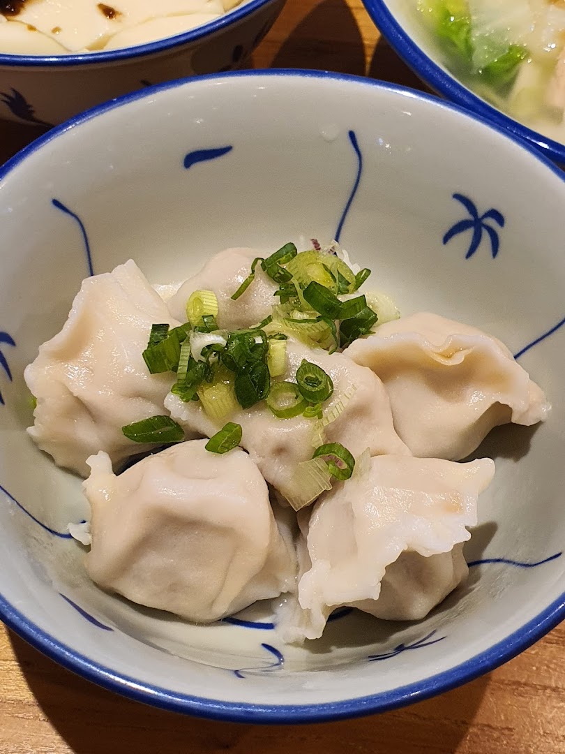 A close-up of a bowl of freshly steamed dumplings topped with chopped green onions.