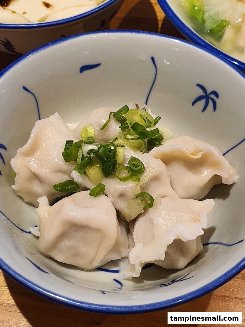 A close-up of a bowl of freshly steamed dumplings topped with chopped green onions.