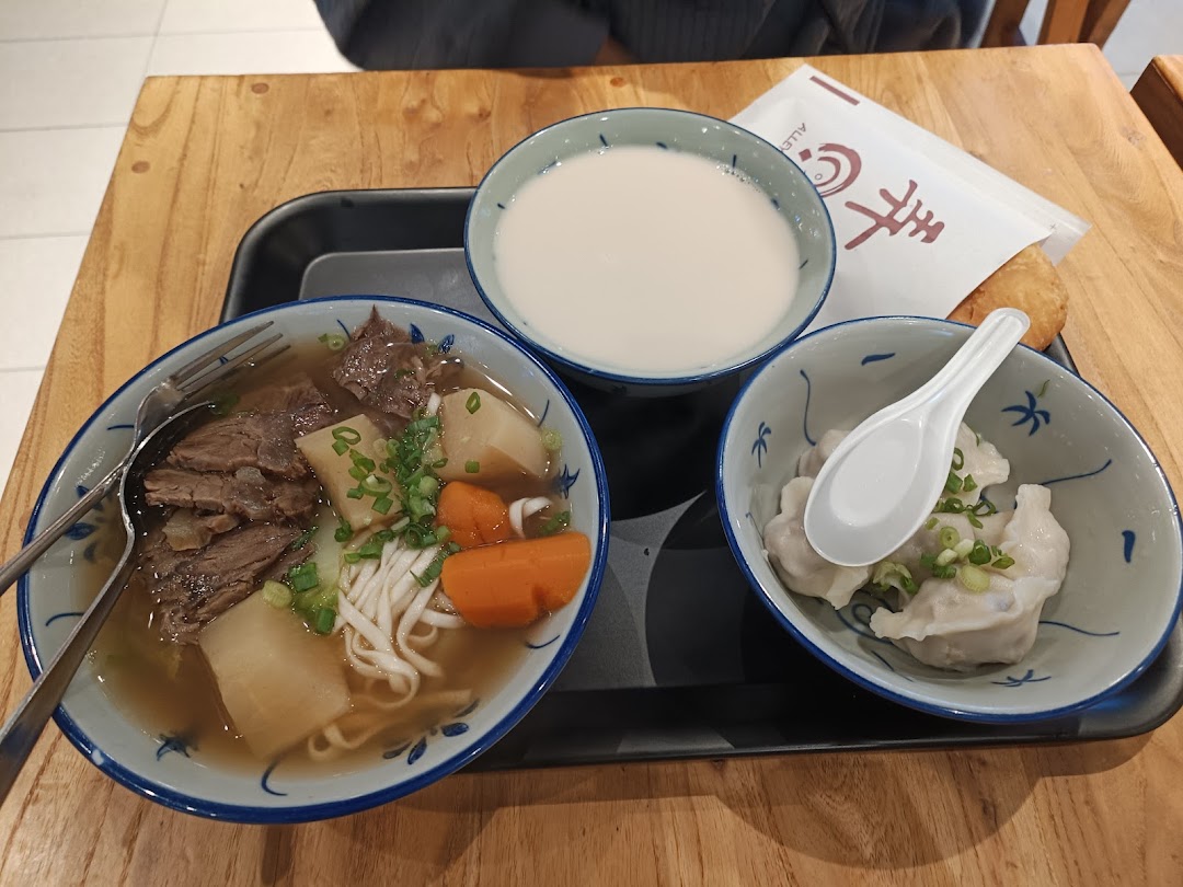 A delicious meal set featuring beef noodle soup, dumplings, and a drink on a wooden table.