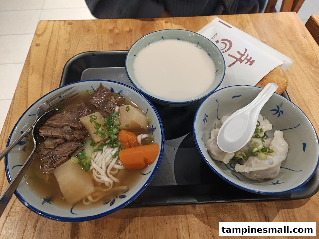 A delicious meal set featuring beef noodle soup, dumplings, and a drink on a wooden table.