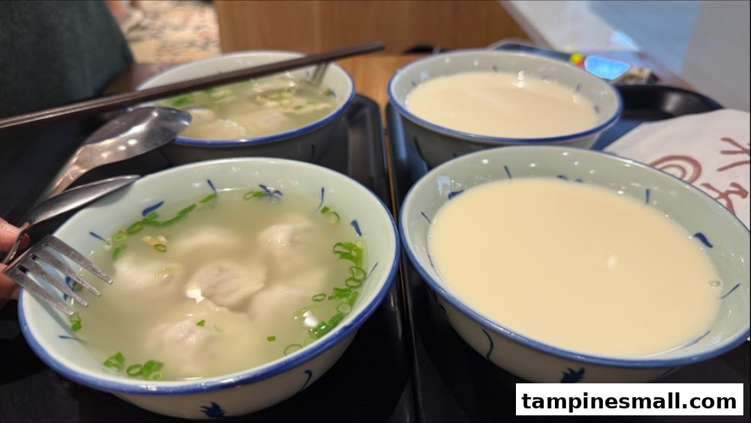 Four bowls of food and drinks, including dumplings/wontons and soy milk, served on trays.