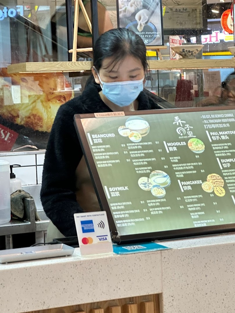 A staff member stands behind a counter with a detailed menu board displaying various Asian dishes and drinks.