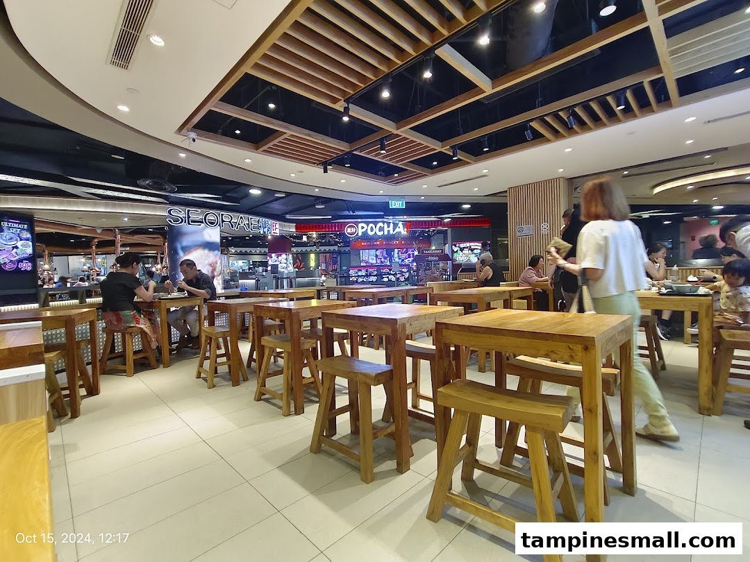 A bustling interior view of a modern dining area with wooden tables and patrons enjoying meals.