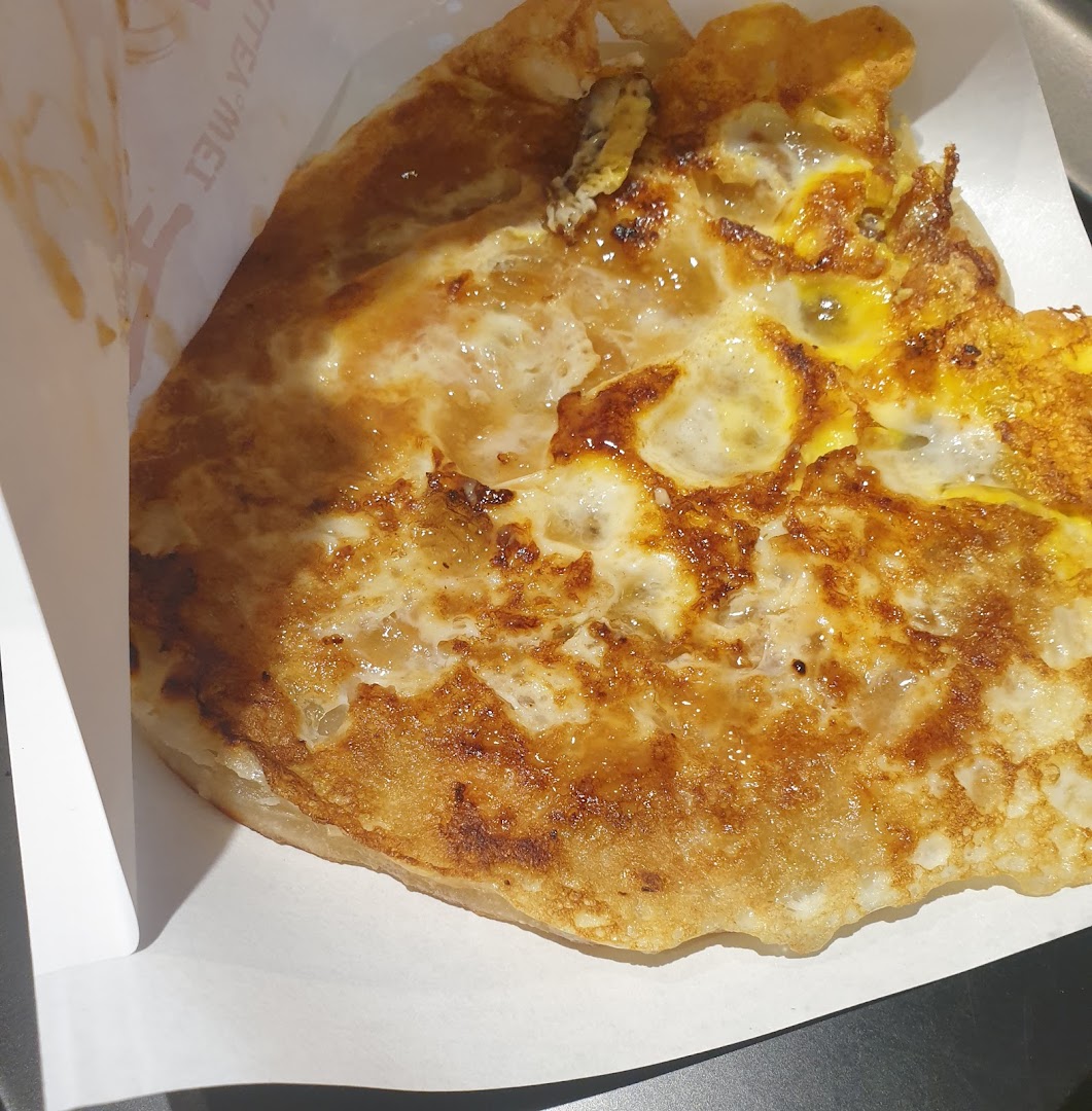A close-up of a golden-brown fried pancake with egg, served in a paper holder.