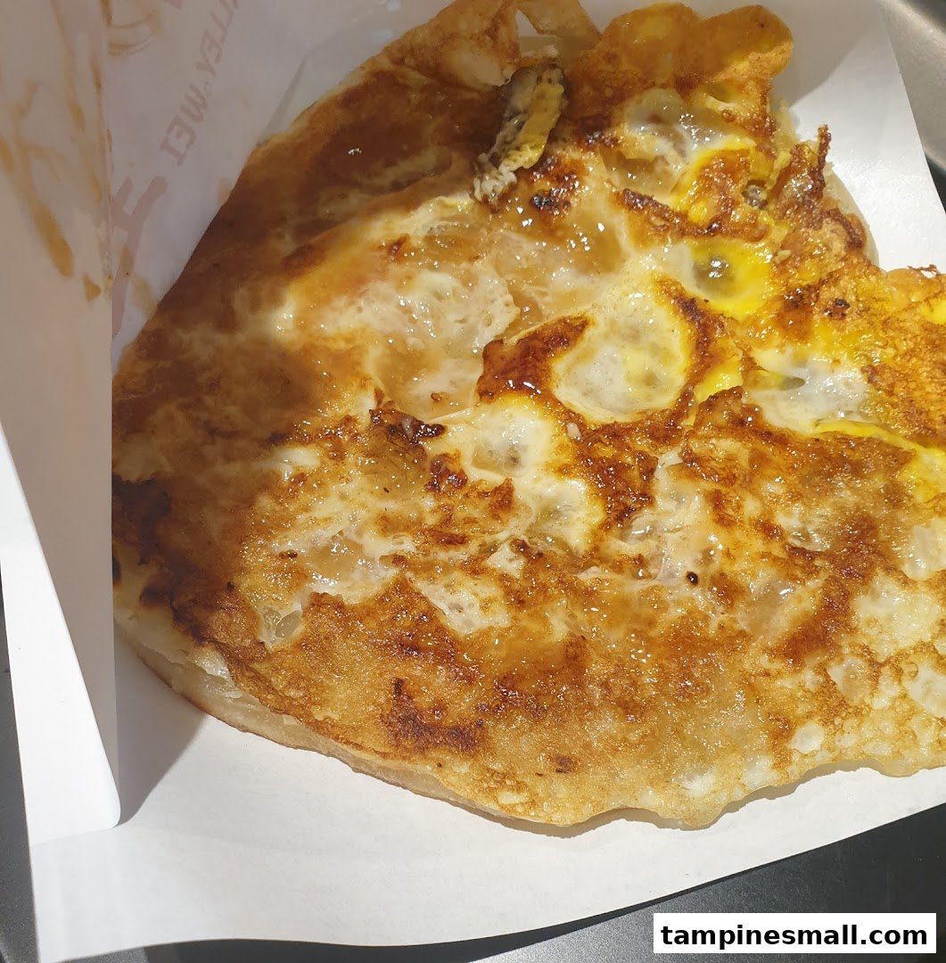 A close-up of a golden-brown fried pancake with egg, served in a paper holder.