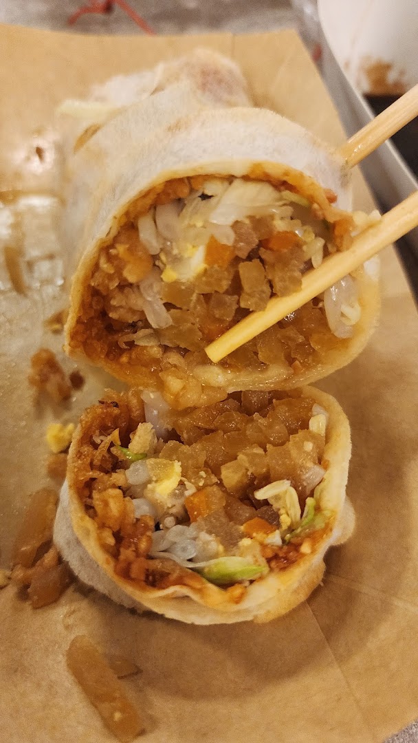 A close-up of a freshly cut popiah, revealing its savory fillings, held by chopsticks.