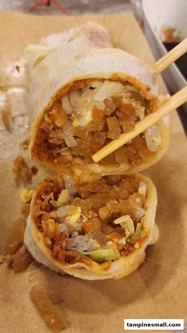 A close-up of a freshly cut popiah, revealing its savory fillings, held by chopsticks.