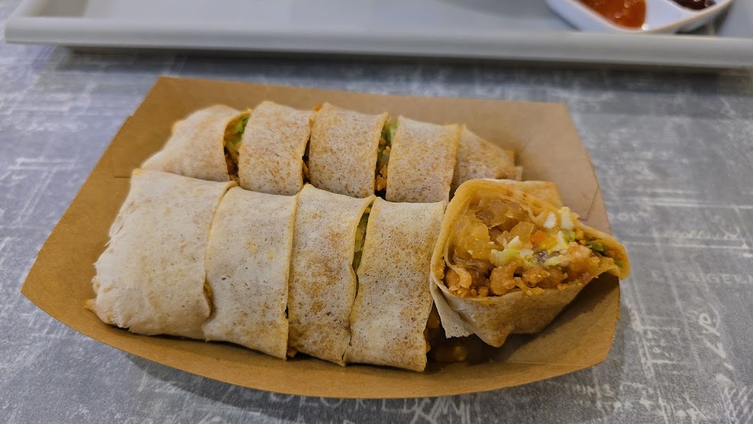 Freshly prepared popiah rolls, sliced and served in a brown paper tray, with one roll showing its delicious filling.
