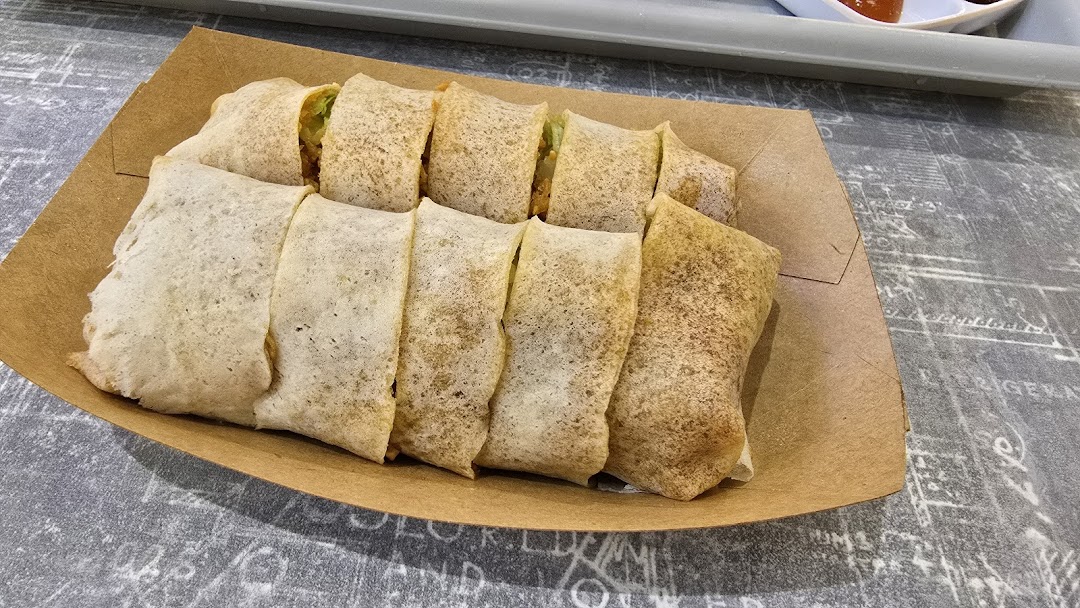 A close-up of freshly prepared popiah rolls served in a brown paper tray.