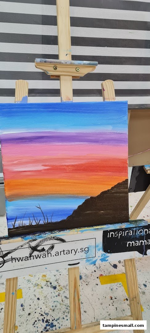 A vibrant landscape painting on an easel, showcasing a colorful sunset over water.