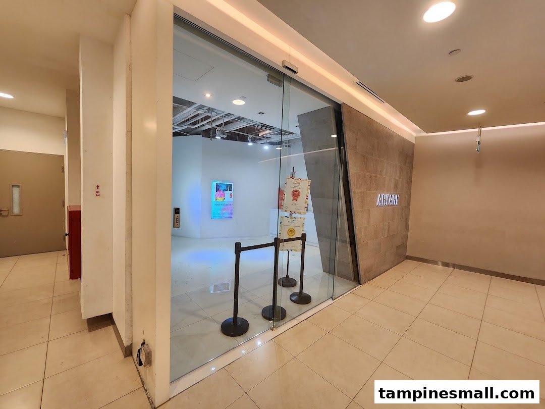 The modern glass entrance of ARTARY Tampines Mall, an art education center, with a tiled wall.