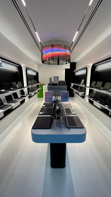 A modern, brightly lit electronics store interior displaying numerous laptops on sleek white and black fixtures.