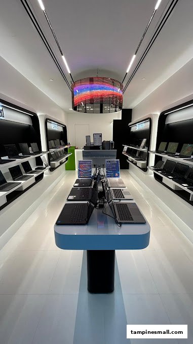 A modern, brightly lit electronics store interior displaying numerous laptops on sleek white and black fixtures.