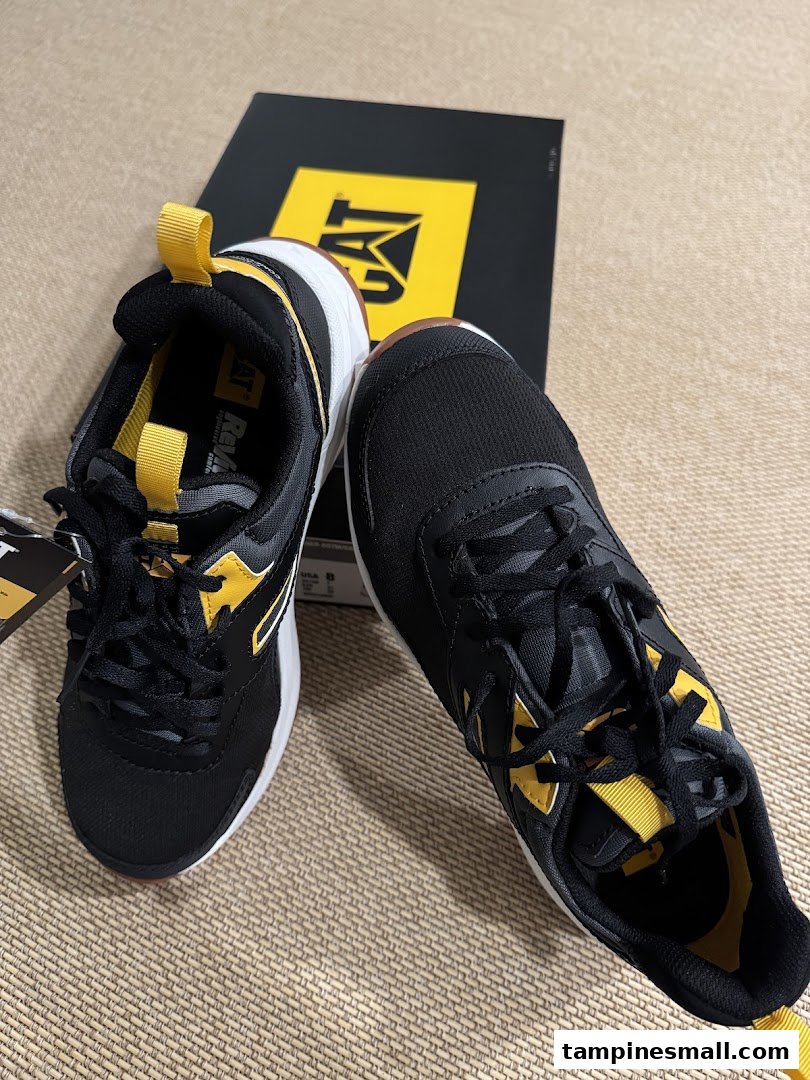 A pair of black and yellow CAT brand sneakers with their shoebox in the background.