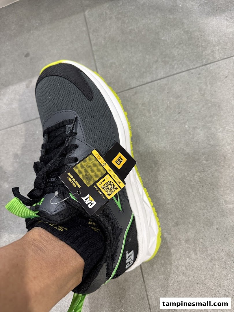 A person's foot wearing a grey and neon green CAT brand sneaker with product tags attached.