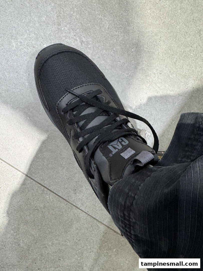 Close-up of a person wearing a black CAT brand shoe on a tiled floor.