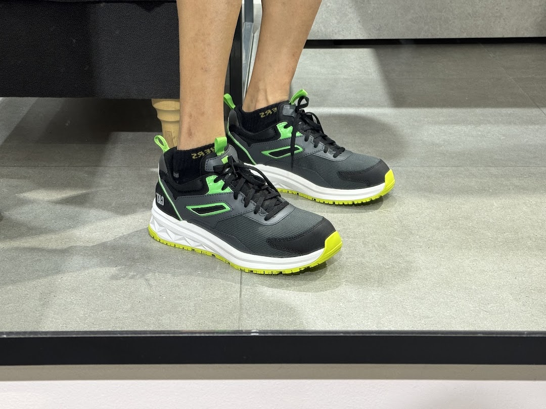 A person models black and neon green Caterpillar sneakers on a grey floor.