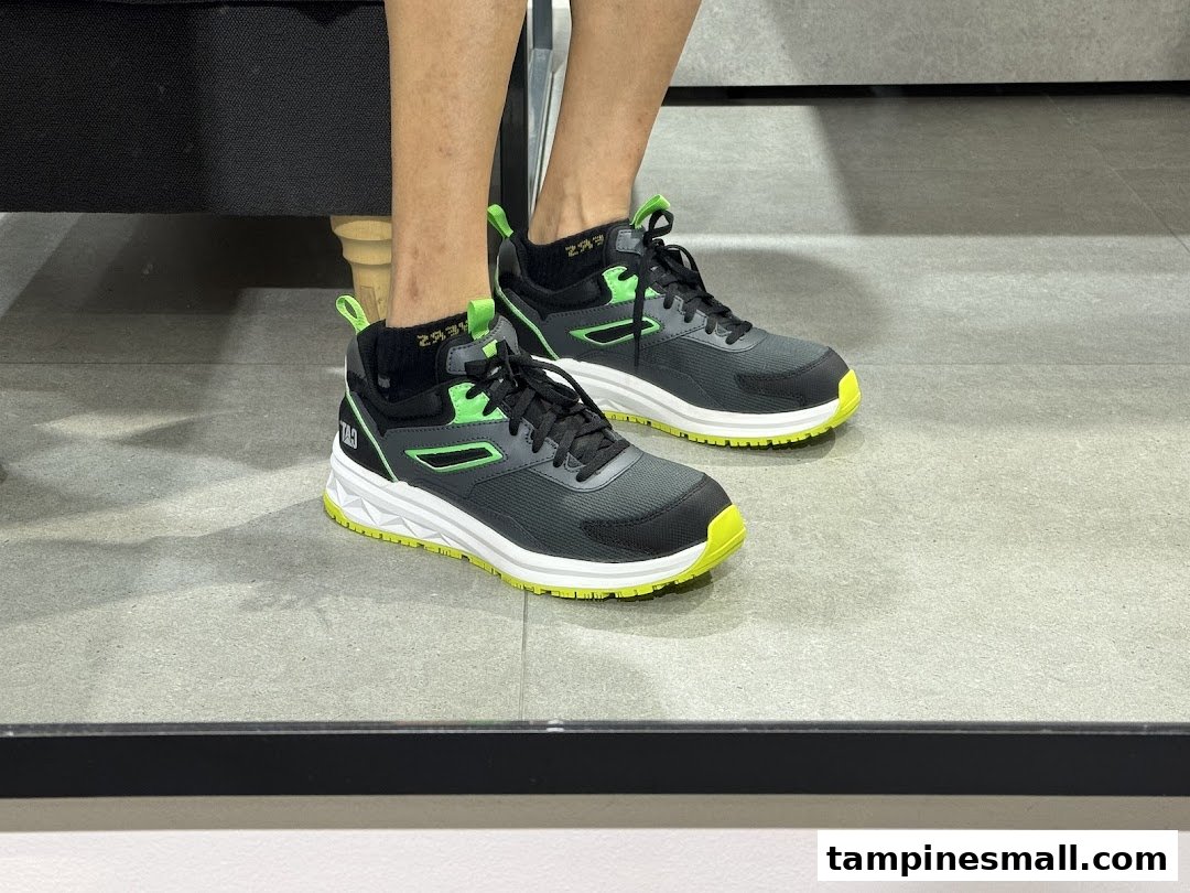 A person models black and neon green Caterpillar sneakers on a grey floor.
