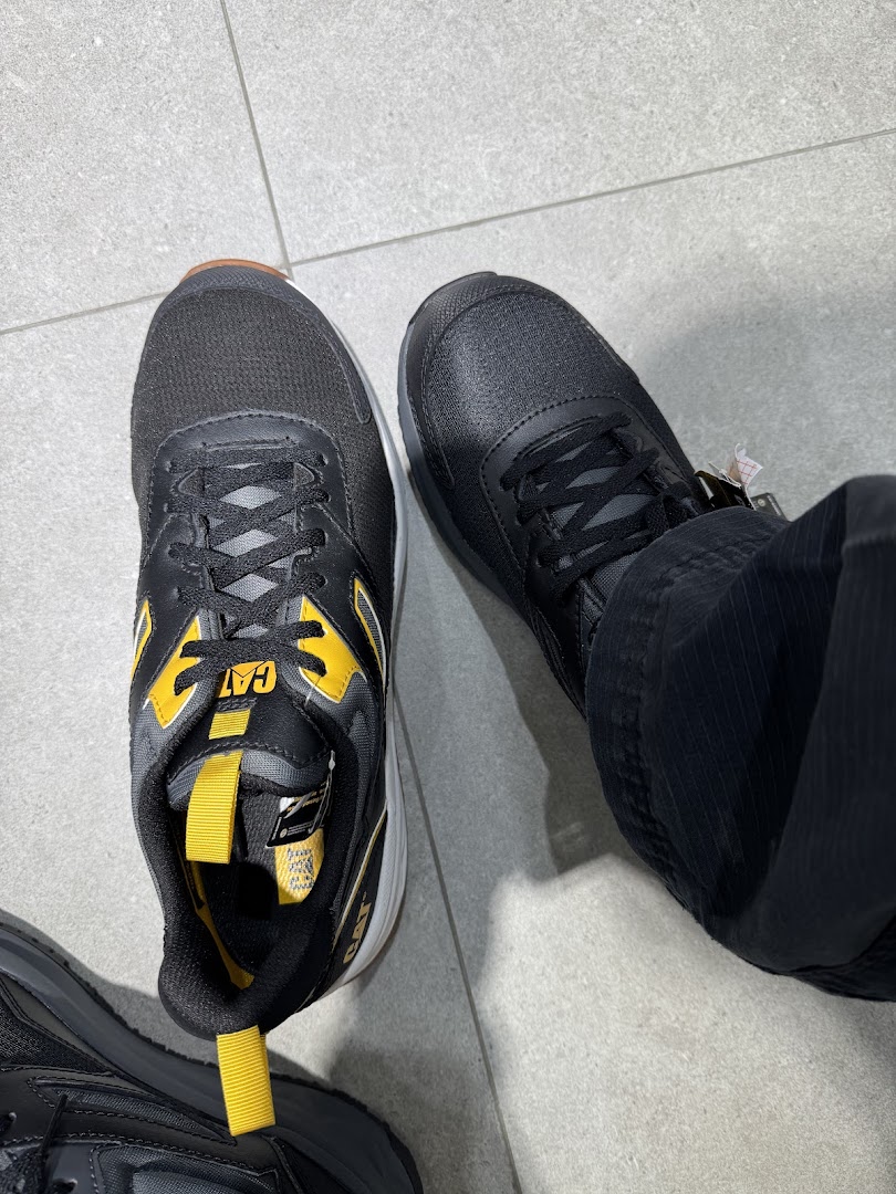 Close-up of a person trying on black and yellow CAT brand sneakers in a store.