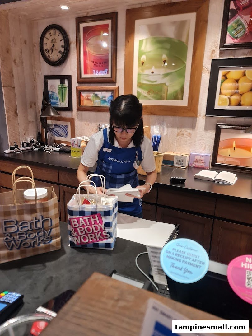 A Bath & Body Works staff member assists a customer at the checkout counter, surrounded by product displays.