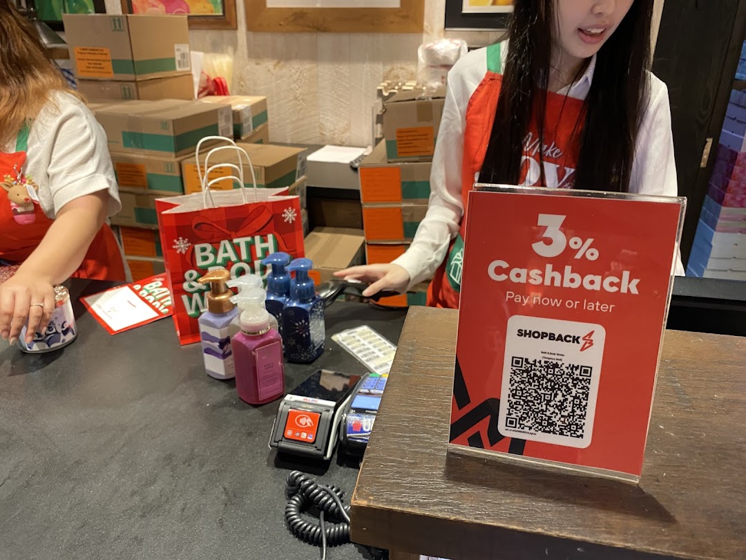 A Bath & Body Works checkout counter with staff, products, and a ShopBack cashback sign.