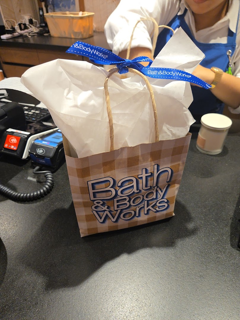 A Bath & Body Works shopping bag with a blue ribbon on a counter, ready for a customer.