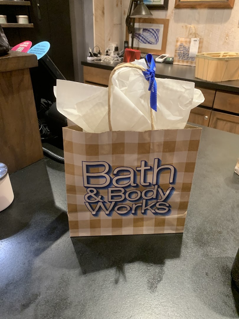 A Bath & Body Works shopping bag with tissue paper and a blue ribbon sits on a store counter.