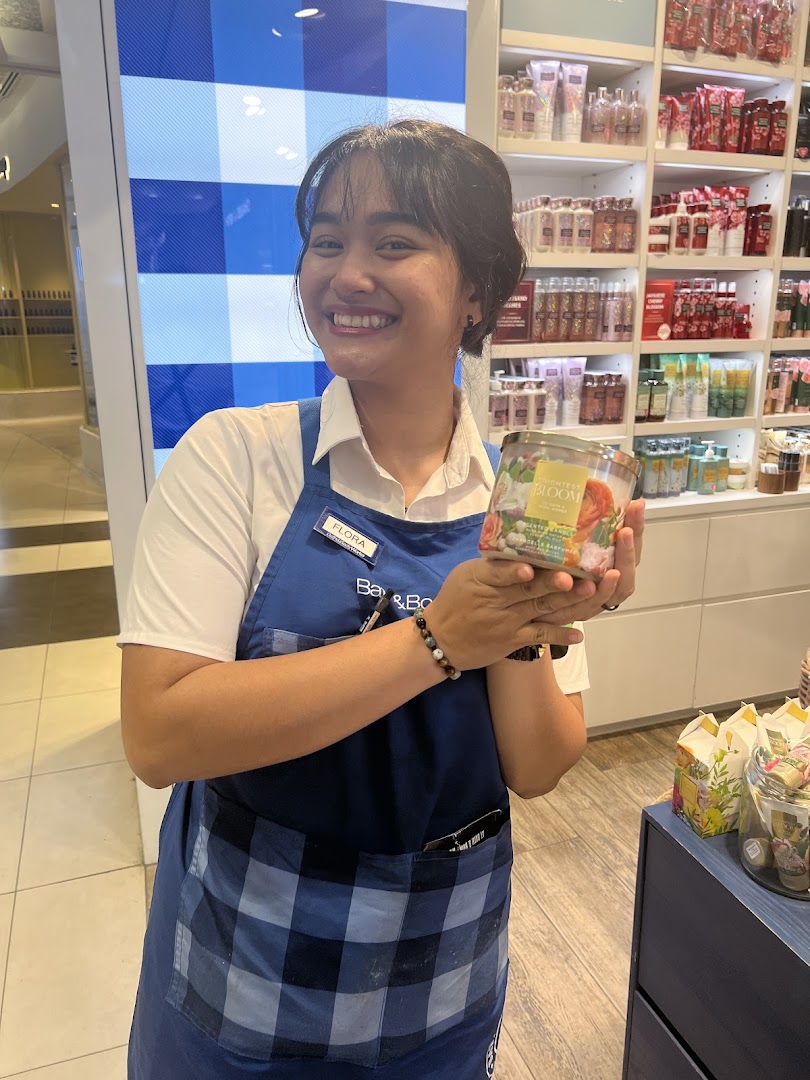 A smiling Bath & Body Works staff member holding a scented candle inside the store.