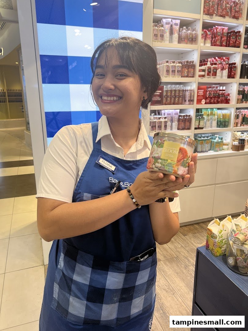 A smiling Bath & Body Works staff member holding a scented candle inside the store.