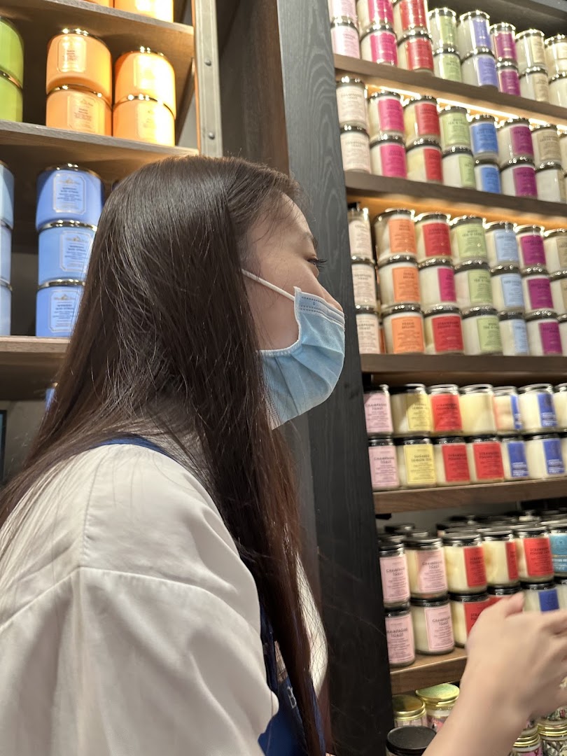 A customer wearing a mask browses colorful candles and body care products on shelves at Bath & Body Works.