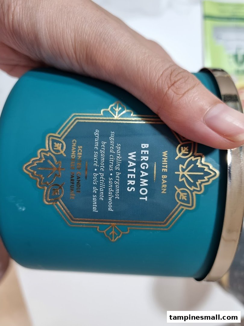 A hand holds a teal Bath & Body Works 'Bergamot Waters' scented candle.