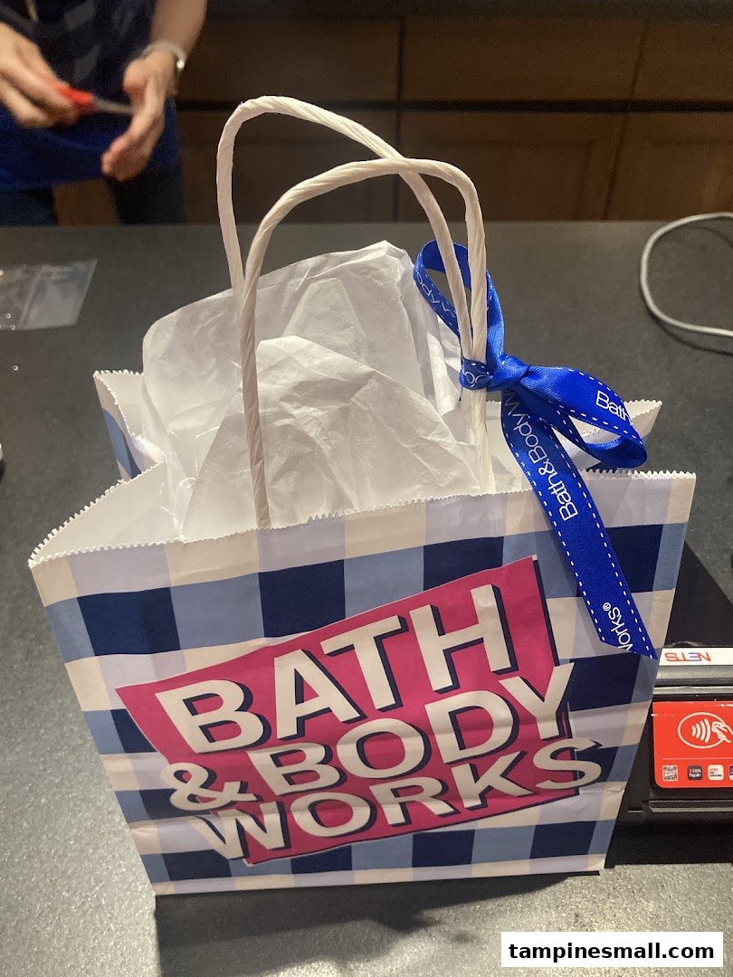 A Bath & Body Works shopping bag, filled with purchases and tied with a blue ribbon, on a store counter.