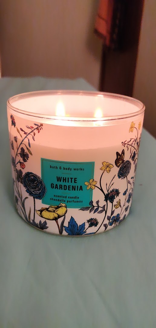 A lit Bath & Body Works 'White Gardenia' three-wick scented candle with a decorative floral design.