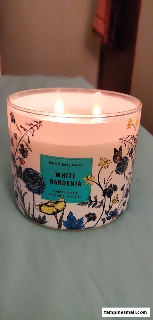 A lit Bath & Body Works 'White Gardenia' three-wick scented candle with a decorative floral design.