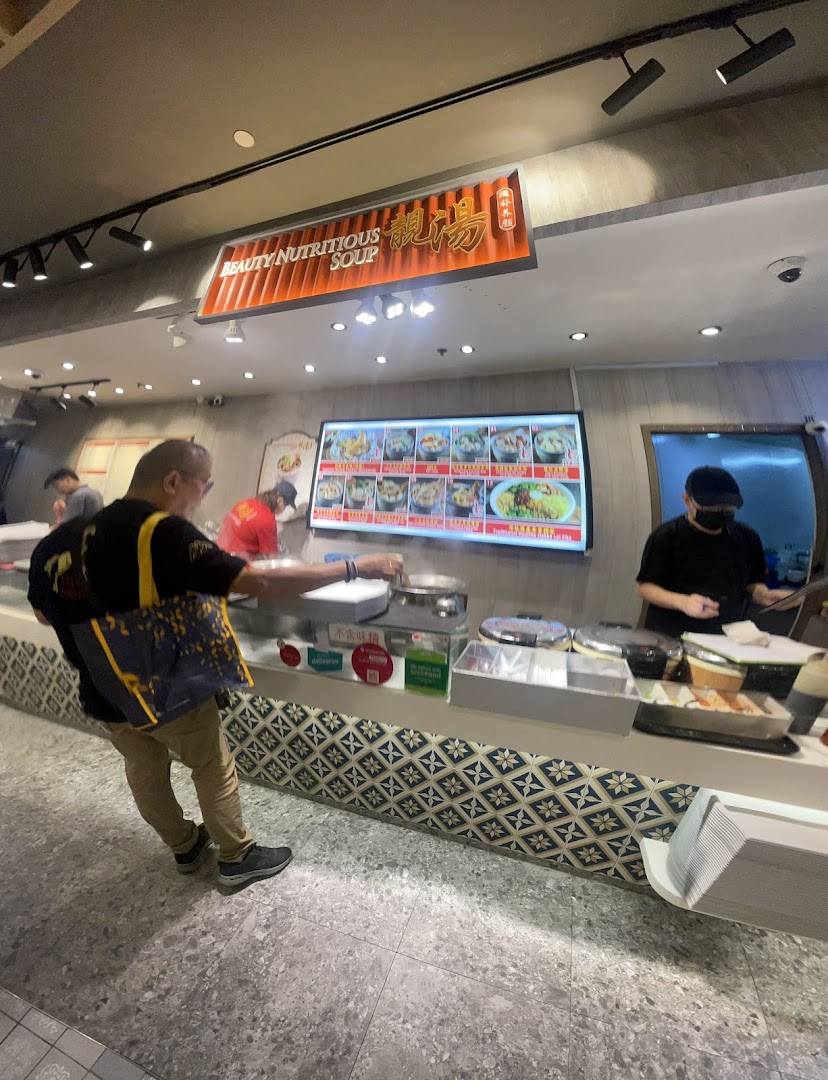 A customer orders at the Beauty Nutritious Soup stall, featuring a digital menu board and counter.