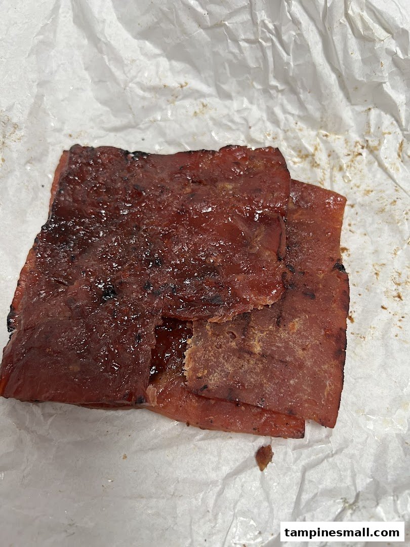 Close-up of glistening, barbecued bak kwa slices from Bee Cheng Hiang on white paper.
