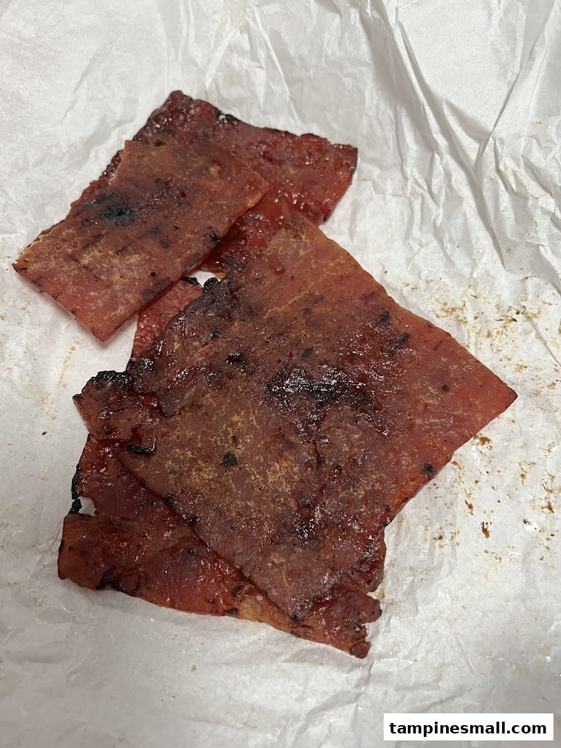 Close-up of several pieces of glossy, grilled bak kwa (BBQ meat slices) resting on white paper.